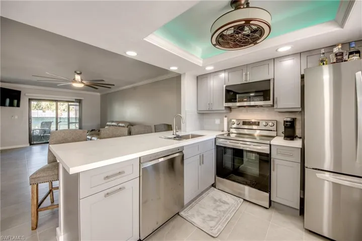 Kitchen with gray cabinetry, stainless steel appliances, light countertops, open floor plan, and ornamental molding