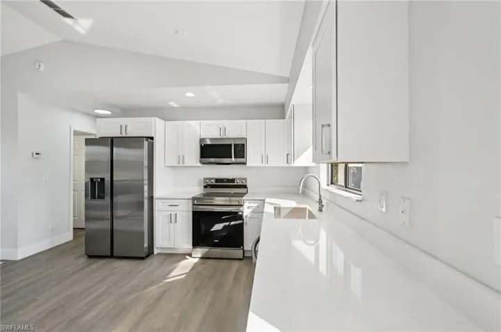 Kitchen with stainless steel appliances, white cabinets, light wood-style floors, lofted ceiling, and light stone counters