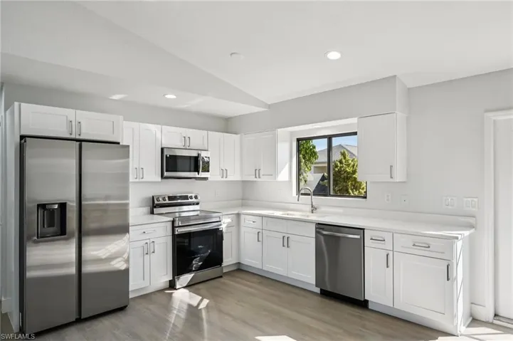 Kitchen featuring stainless steel appliances, white cabinets, vaulted ceiling, light wood-type flooring, and recessed lighting