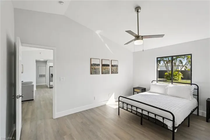 Bedroom featuring light wood finished floors, lofted ceiling, ceiling fan, and stainless steel fridge with ice dispenser