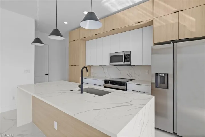 Kitchen with light stone counters, sink, white cabinetry, appliances with stainless steel finishes, and decorative light fixtures
