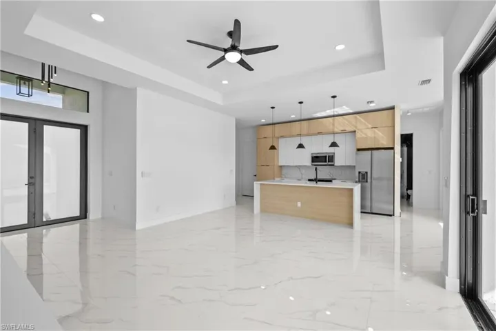 Kitchen with hanging light fixtures, an island with sink, ceiling fan, a tray ceiling, and appliances with stainless steel finishes