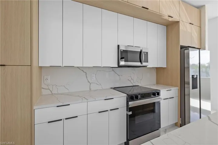 Kitchen featuring white cabinetry, appliances with stainless steel finishes, backsplash, and light stone countertops
