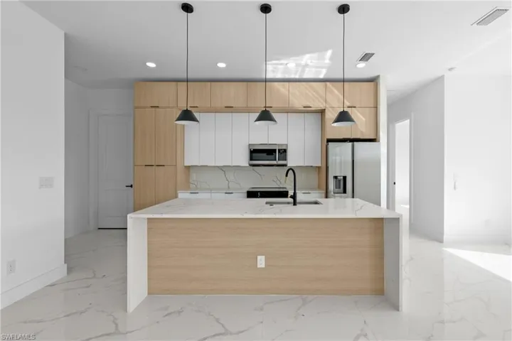 Kitchen with stainless steel appliances, white cabinetry, sink, light stone counters, and decorative light fixtures