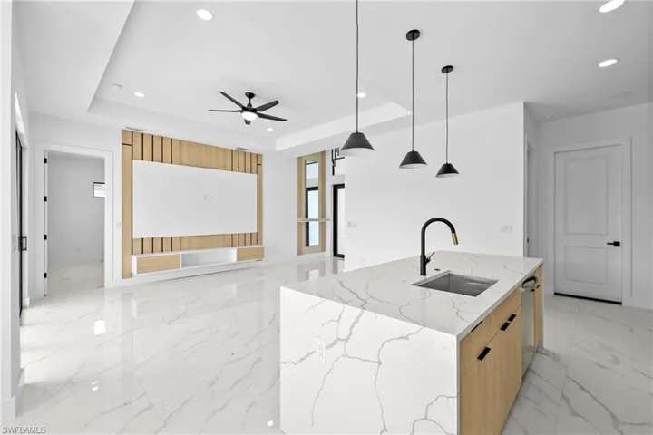 Kitchen featuring a center island with sink, hanging light fixtures, sink, a tray ceiling, and light stone countertops