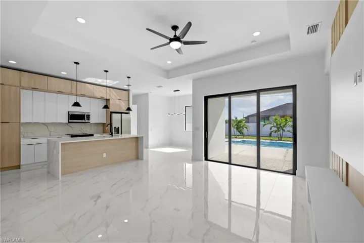 Kitchen with stainless steel appliances, hanging light fixtures, a raised ceiling, white cabinets, and decorative backsplash