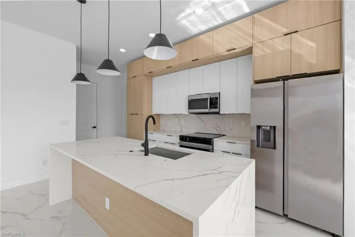 Kitchen featuring white cabinetry, a center island with sink, light stone counters, appliances with stainless steel finishes, and hanging light fixtures