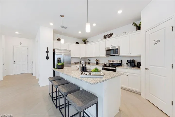 Kitchen featuring a kitchen bar, stainless steel appliances, white cabinetry, a center island with sink, and decorative light fixtures