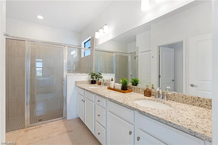 Full bathroom featuring double vanity, a stall shower, and light tile patterned floors