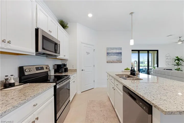 Kitchen featuring stainless steel appliances, white cabinets, a center island with sink, light stone countertops, and ceiling fan