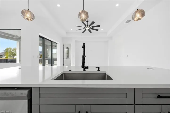 Kitchen with stainless steel dishwasher, decorative light fixtures, gray cabinetry, ceiling fan, and a tray ceiling