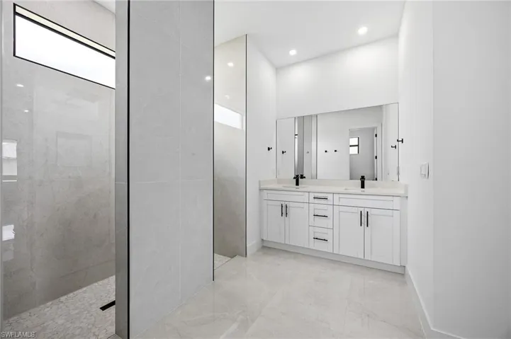 Full bathroom with double vanity, a marble finish shower, recessed lighting, and light marble finish flooring