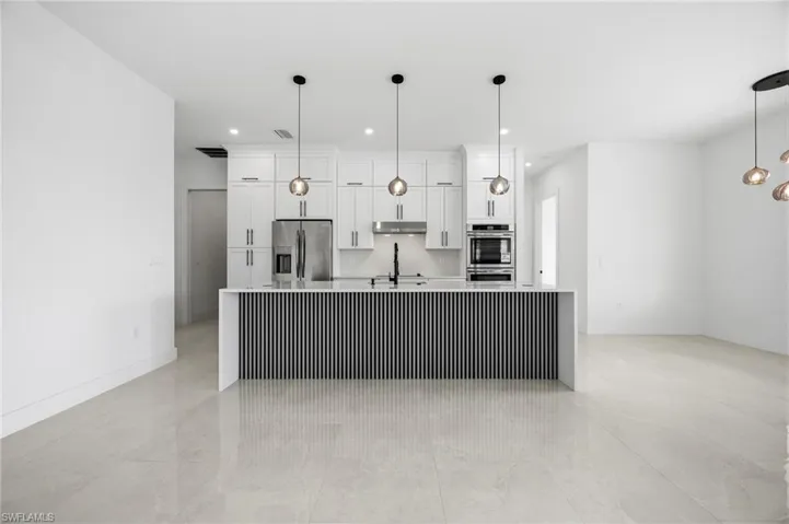 Kitchen featuring white cabinetry, a large island, stainless steel appliances, light stone counters, and pendant lighting