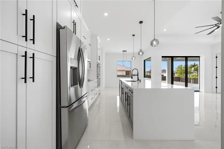 Kitchen with stainless steel refrigerator with ice dispenser, pendant lighting, a large island, light stone counters, and dual tone cabinets
