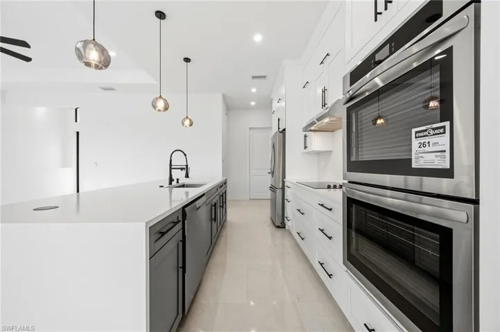 Kitchen with stainless steel appliances, dual tone cabinets, hanging light fixtures, light stone countertops, and a kitchen island with sink