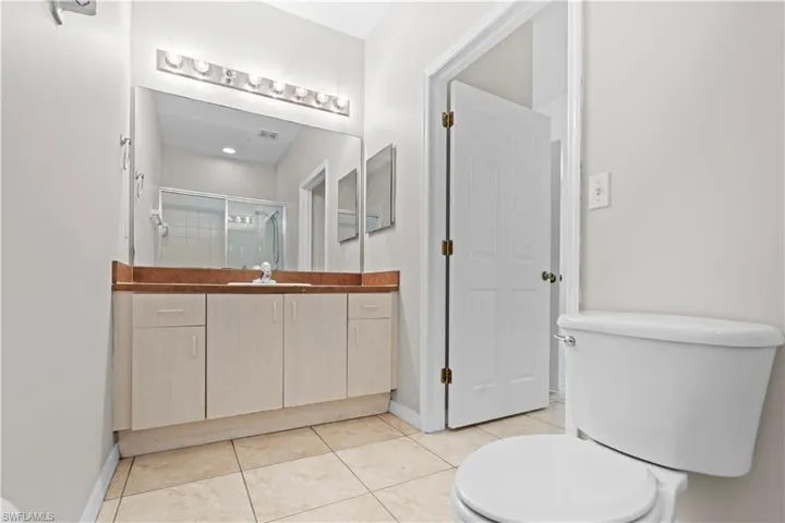 Bathroom with baseboards, toilet, vanity, tile patterned floors, and a stall shower