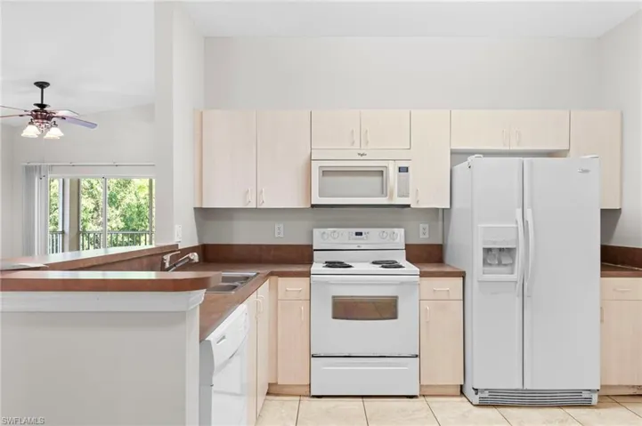 Kitchen with white appliances, a ceiling fan, a peninsula, and dark countertops