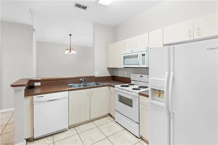 Kitchen with white appliances, a peninsula, dark countertops, visible vents, and a sink