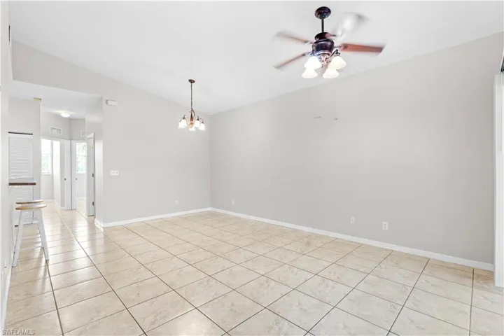 Spare room with ceiling fan with notable chandelier, light tile patterned floors, visible vents, vaulted ceiling, and baseboards
