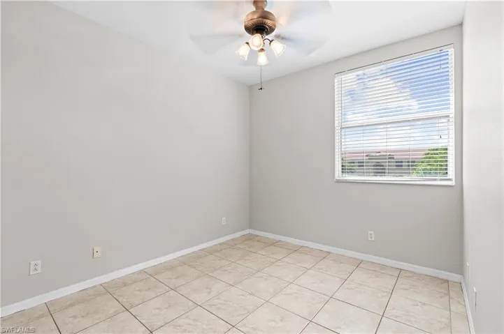 Empty room with light tile patterned floors, baseboards, and a ceiling fan
