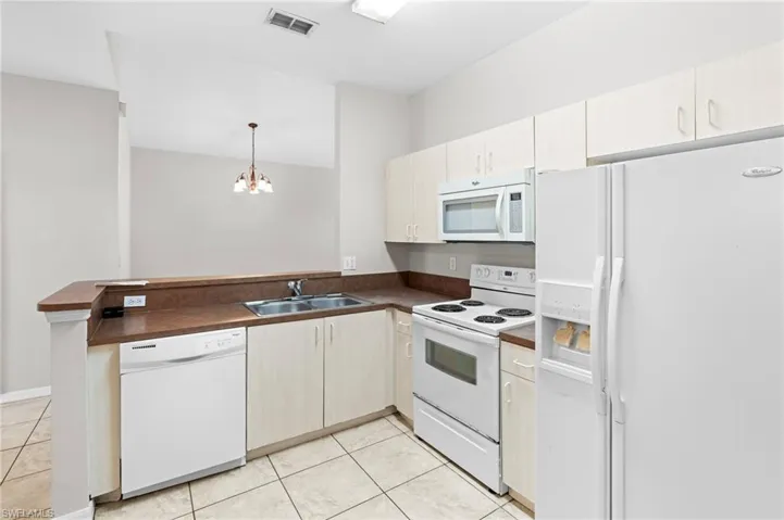 Kitchen with white appliances, a peninsula, dark countertops, visible vents, and a sink