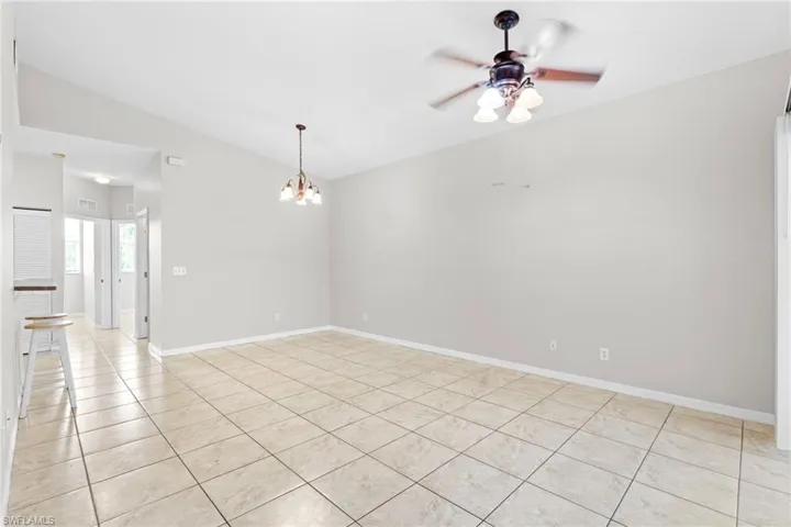 Spare room with visible vents, baseboards, vaulted ceiling, ceiling fan with notable chandelier, and light tile patterned flooring