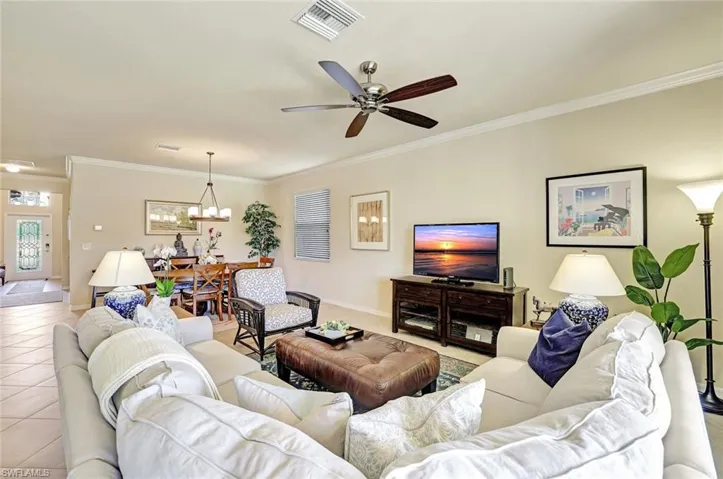 Living room with crown molding, ceiling fan with notable chandelier, and light tile patterned floors