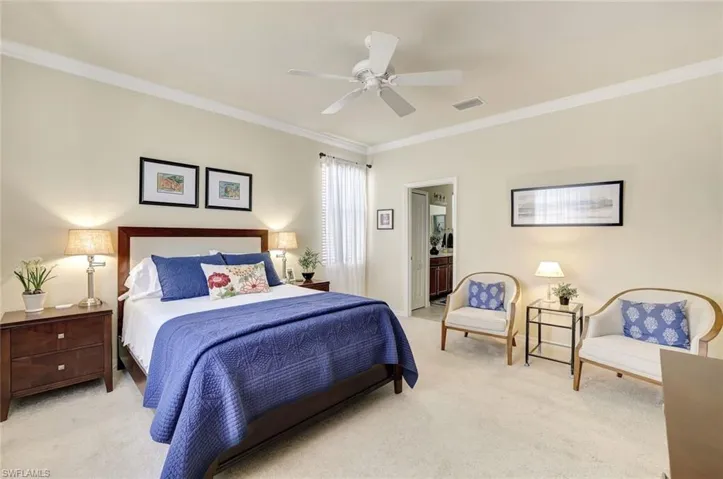 Carpeted bedroom with crown molding, ceiling fan, and ensuite bath