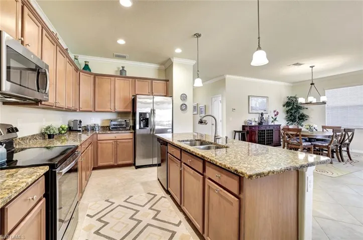 Kitchen with sink, crown molding, appliances with stainless steel finishes, a center island with sink, and decorative light fixtures