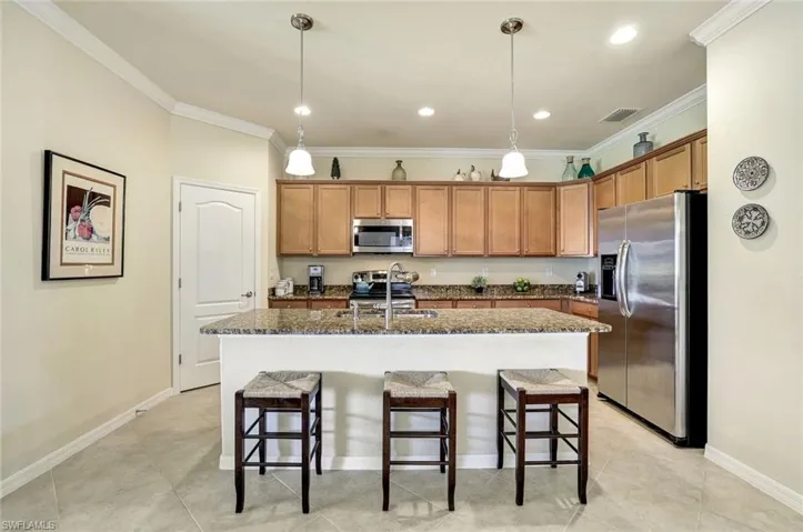 Kitchen with appliances with stainless steel finishes, decorative light fixtures, a kitchen breakfast bar, crown molding, and a center island with sink