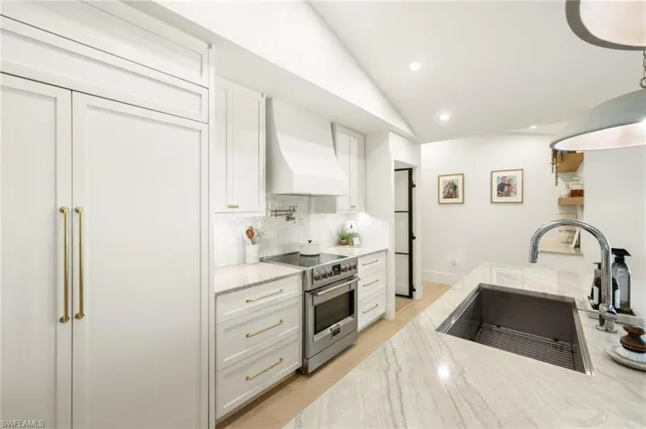Kitchen featuring stainless steel electric range oven, wall chimney range hood, white cabinetry, tasteful backsplash, and light stone countertops