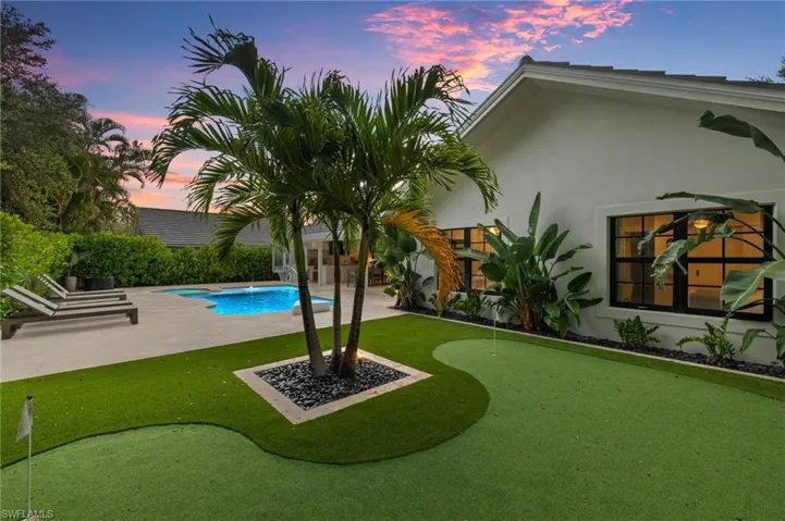 Yard at dusk with a putting green, a patio area, and an outdoor pool