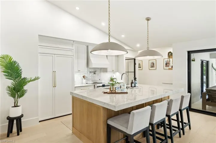 Kitchen with paneled built in fridge, premium range hood, backsplash, light wood finished floors, and a kitchen island with sink