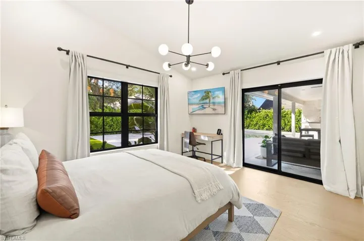 Bedroom with multiple windows, access to outside, vaulted ceiling, a chandelier, and light wood-style floors