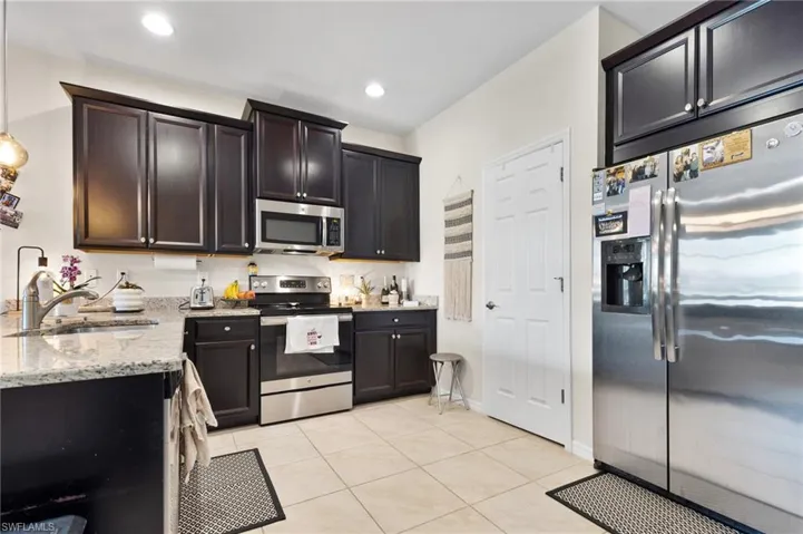 Kitchen featuring dark brown cabinetry, sink, light tile patterned floors, appliances with stainless steel finishes, and light stone countertops