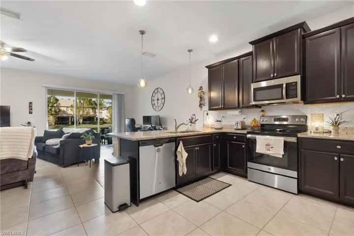 Kitchen with light tile patterned flooring, sink, hanging light fixtures, kitchen peninsula, and stainless steel appliances