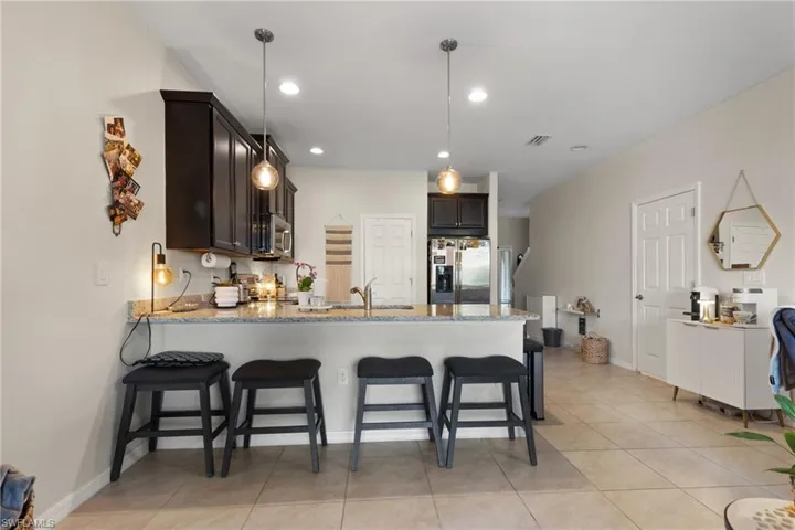 Kitchen with sink, light stone counters, appliances with stainless steel finishes, kitchen peninsula, and pendant lighting