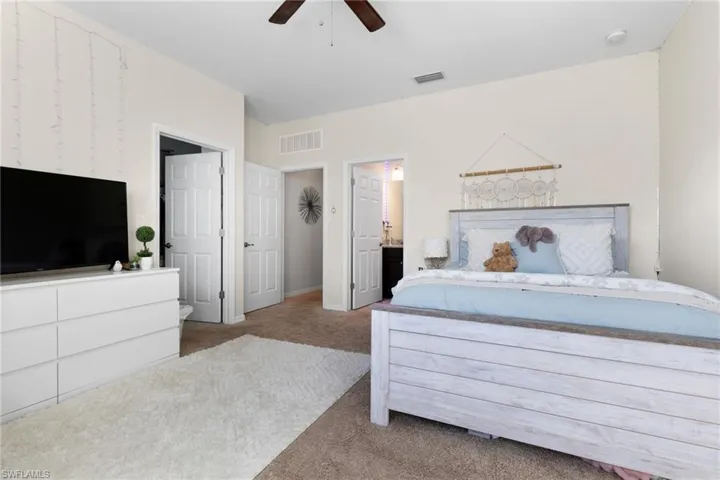 Bedroom with ensuite bath, light colored carpet, and ceiling fan
