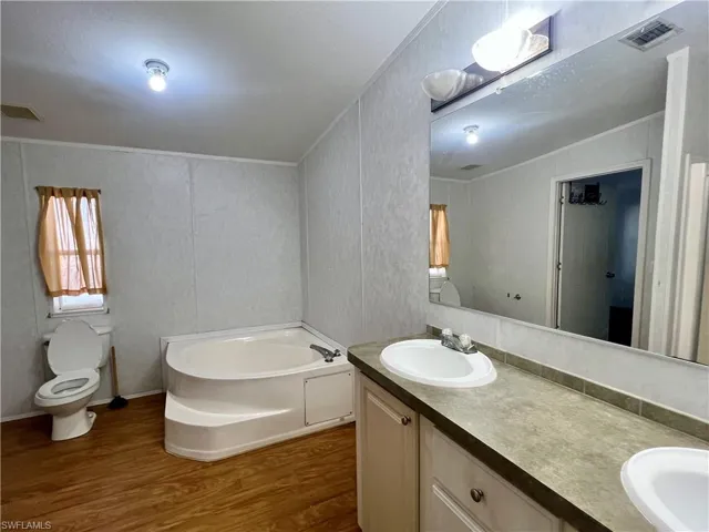 Bathroom featuring a garden tub, dark wood finished floors, double vanity, a decorative wall, and ornamental molding