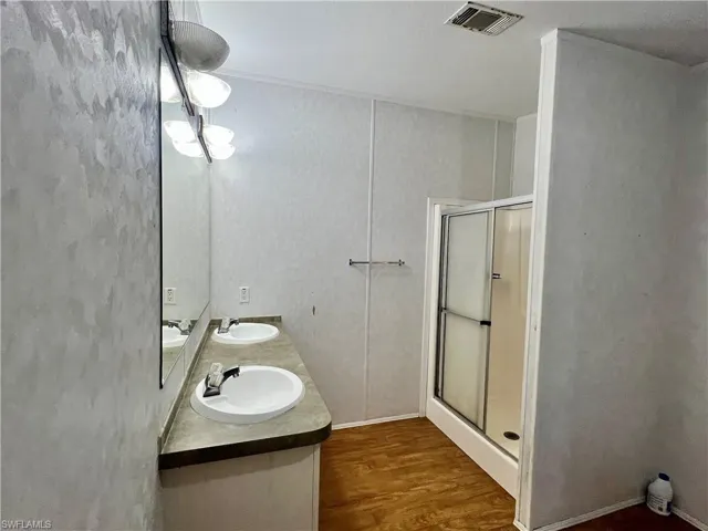 Full bath with a shower stall, dark wood-type flooring, and double vanity