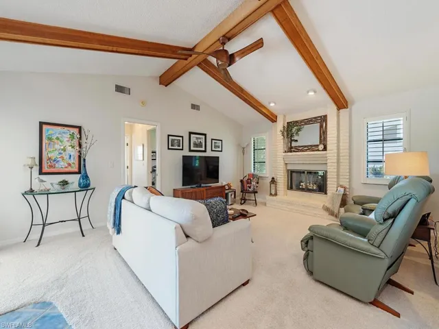 Carpeted living room featuring a fireplace, baseboards, vaulted ceiling with beams, and visible vents