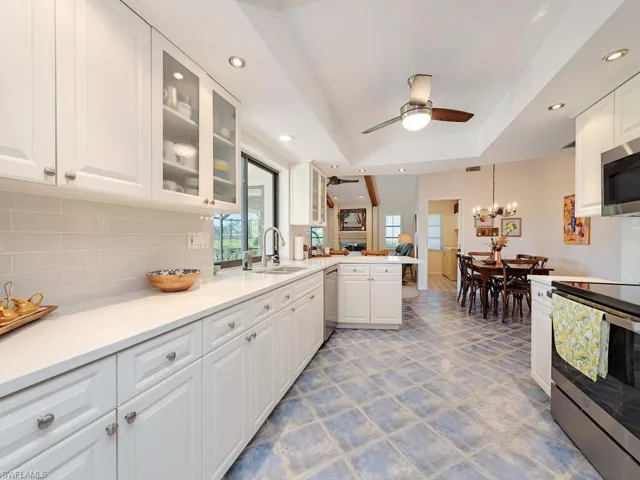Kitchen featuring a peninsula, stainless steel appliances, a raised ceiling, a sink, and ceiling fan with notable chandelier
