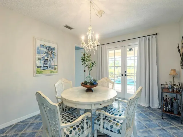 Dining space with french doors, baseboards, a chandelier, a textured ceiling, and visible vents