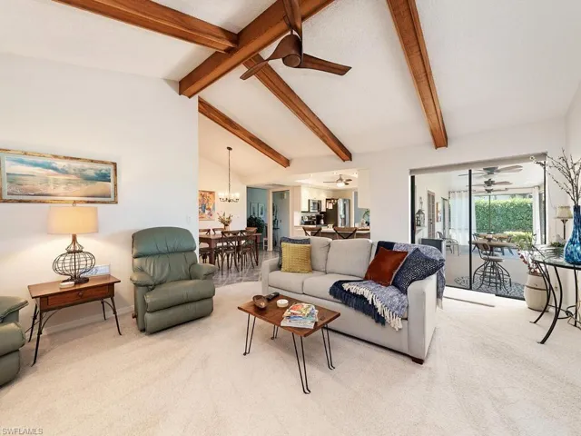 Living area with high vaulted ceiling, baseboards, beam ceiling, ceiling fan with notable chandelier, and light colored carpet