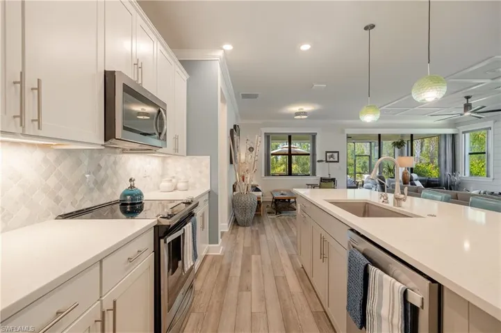 Kitchen featuring crown molding, light wood-type flooring, hanging light fixtures, sink, and appliances with stainless steel finishes