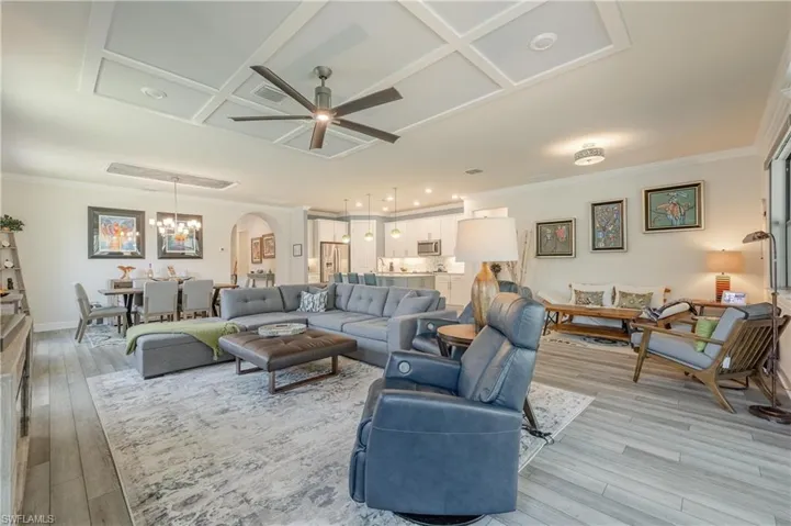 Living room featuring crown molding, coffered ceiling, light wood-type flooring, and ceiling fan with notable chandelier