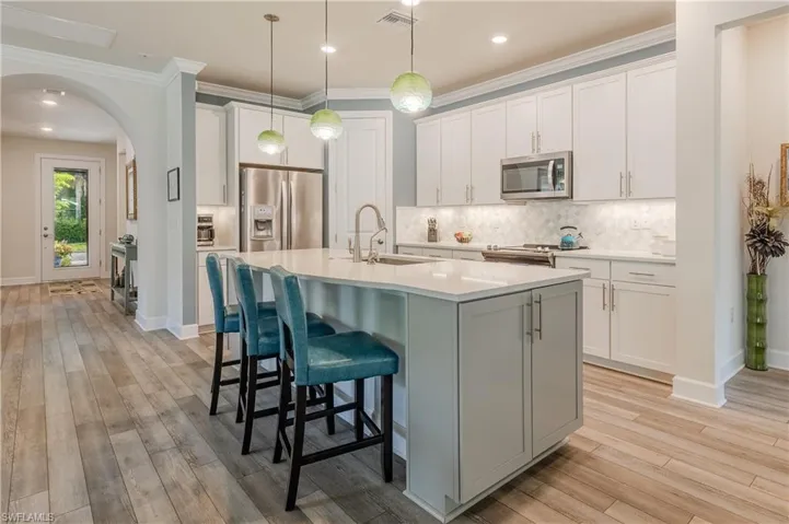 Kitchen with light hardwood / wood-style flooring, stainless steel appliances, white cabinetry, an island with sink, and sink