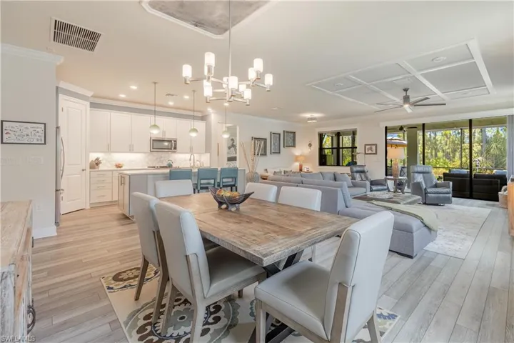 Dining space with light hardwood / wood-style floors, ornamental molding, coffered ceiling, and ceiling fan with notable chandelier
