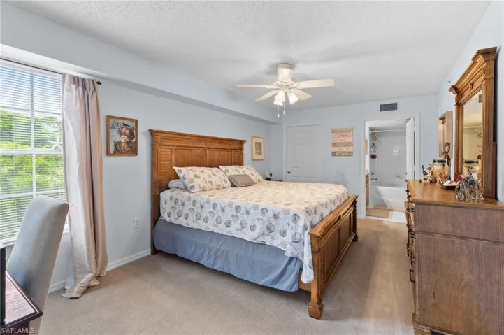Bedroom with carpet, ensuite bath, ceiling fan, and a textured ceiling