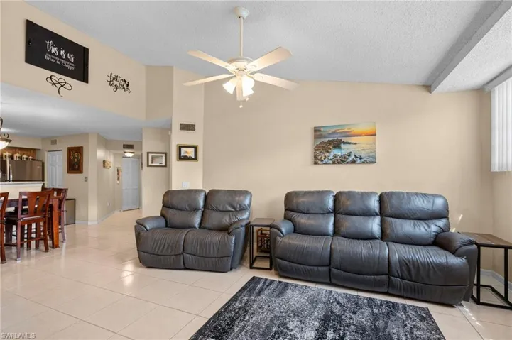 Living room with a textured ceiling, vaulted ceiling, ceiling fan, and light tile patterned floors
